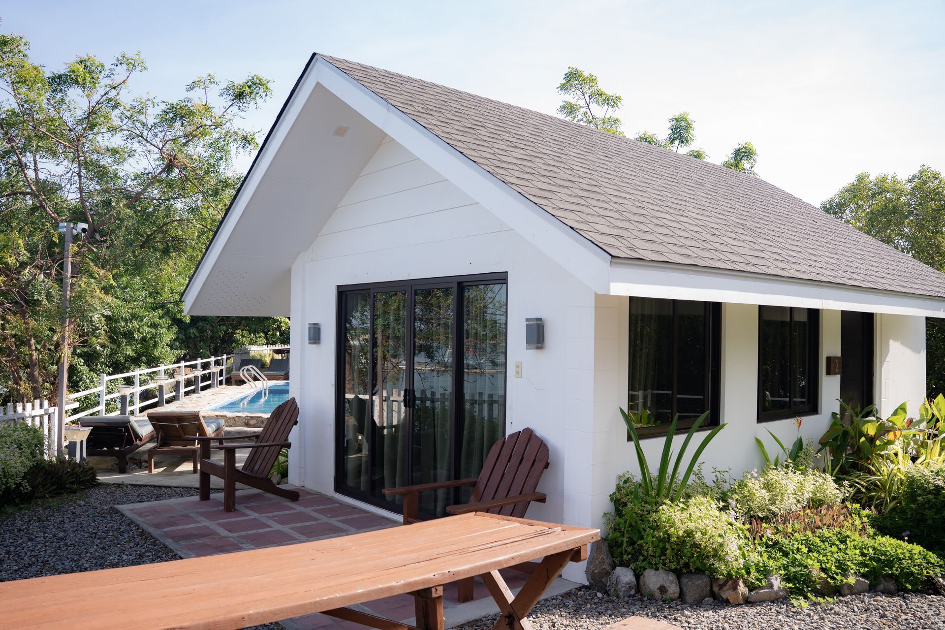 White cottage with a brown roof and a wooden deck overlooking a hot tub.