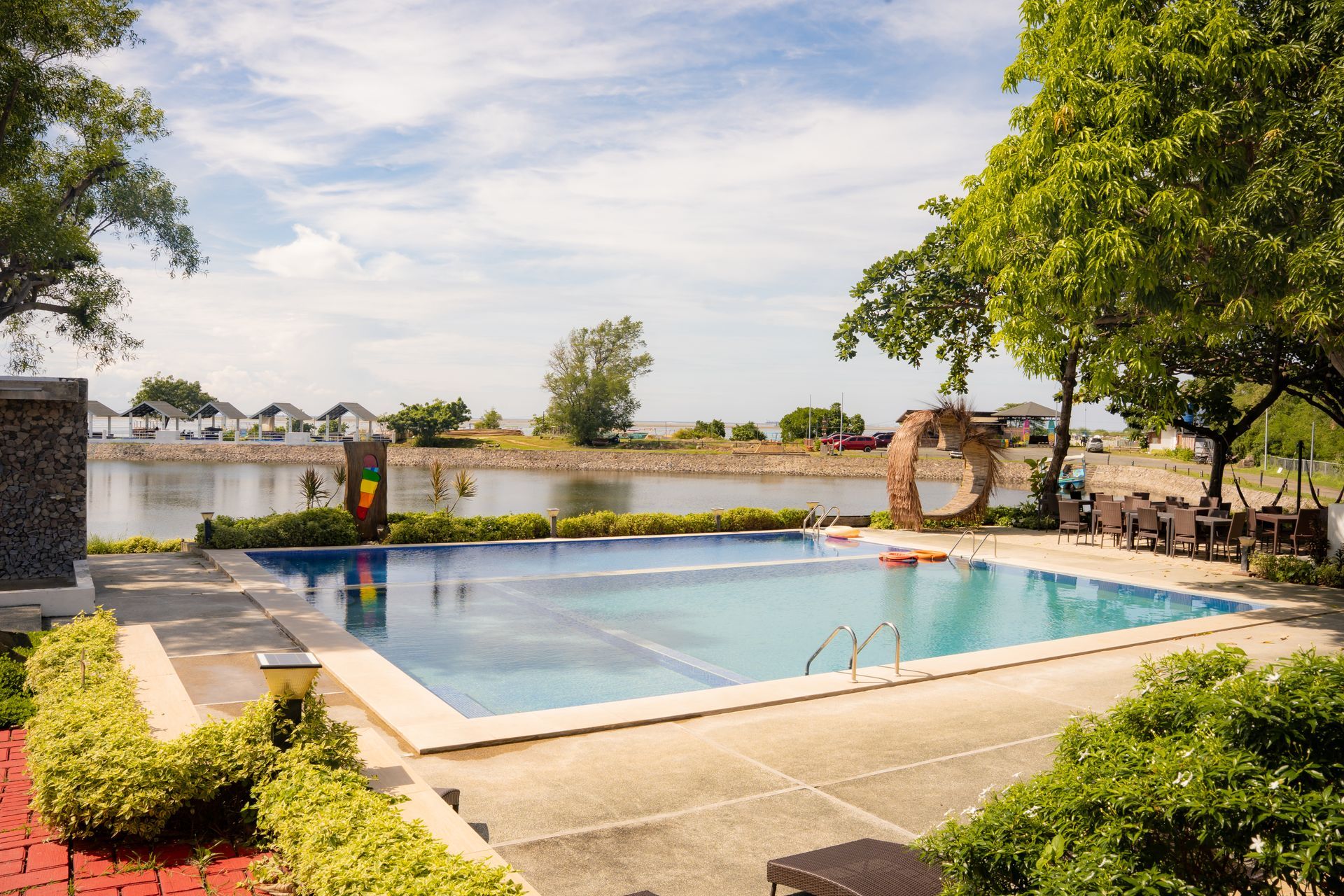Swimming pool overlooking a body of water and distant buildings under a sunny sky.