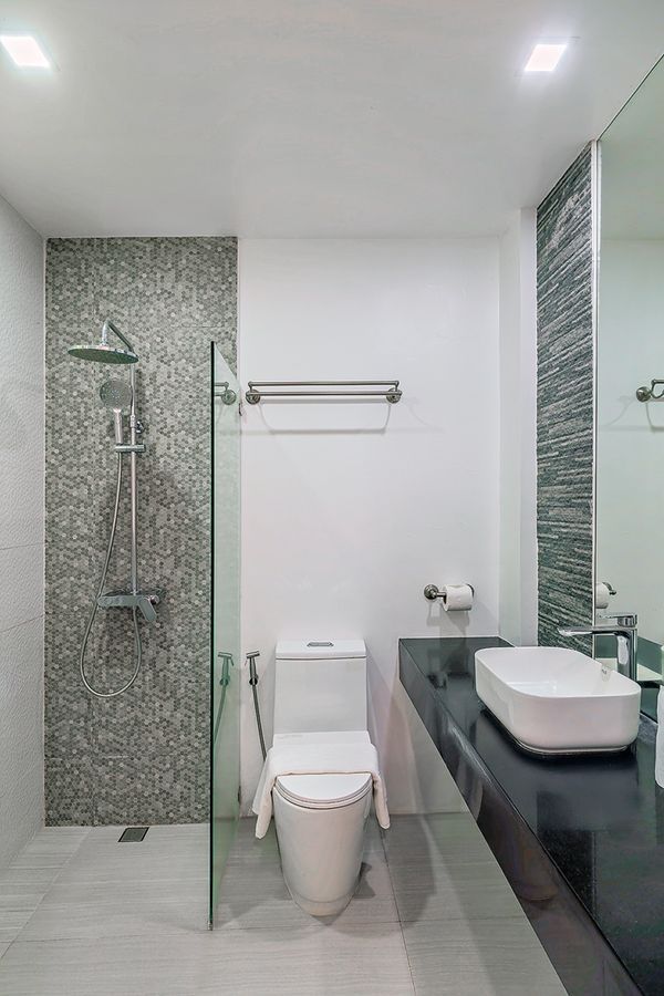 Modern bathroom with white walls, gray tile shower, toilet, and a black countertop with a white sink.