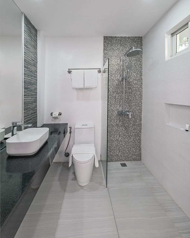 Modern bathroom with a white sink, toilet, and shower with grey tile accents.