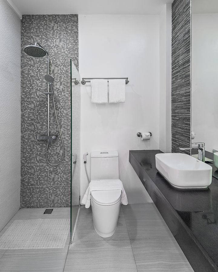 Modern bathroom with gray tile shower, white toilet, and black countertop with a white sink.