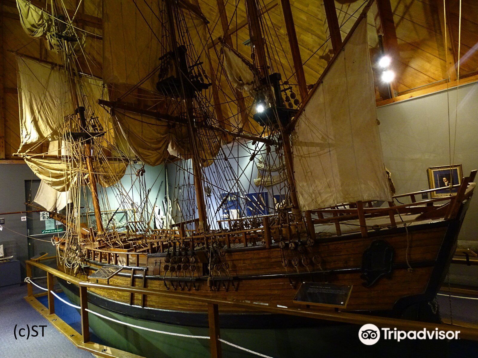 Indoor museum exhibit of a wooden sailing ship with tall masts and rigging on display, lit warmly