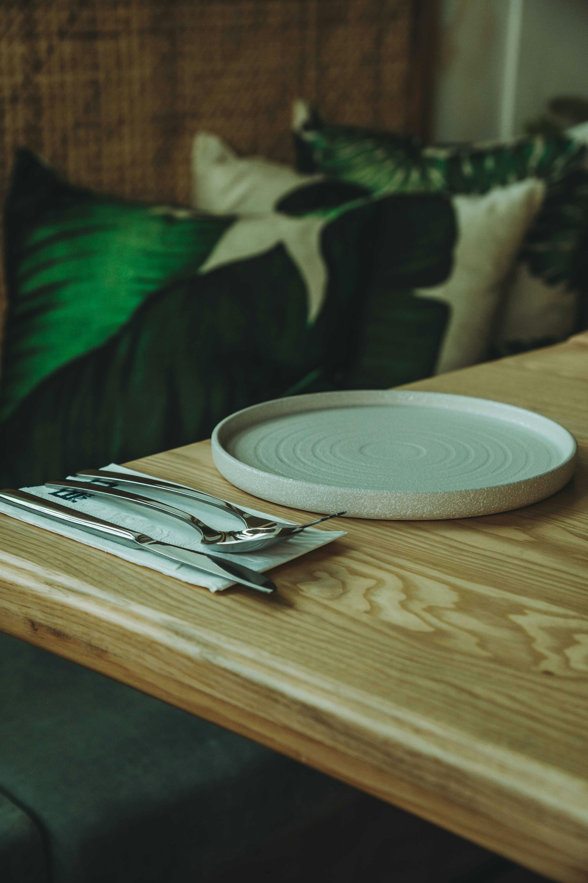 Wooden table with a white plate and folded napkins on a dark sofa backdrop