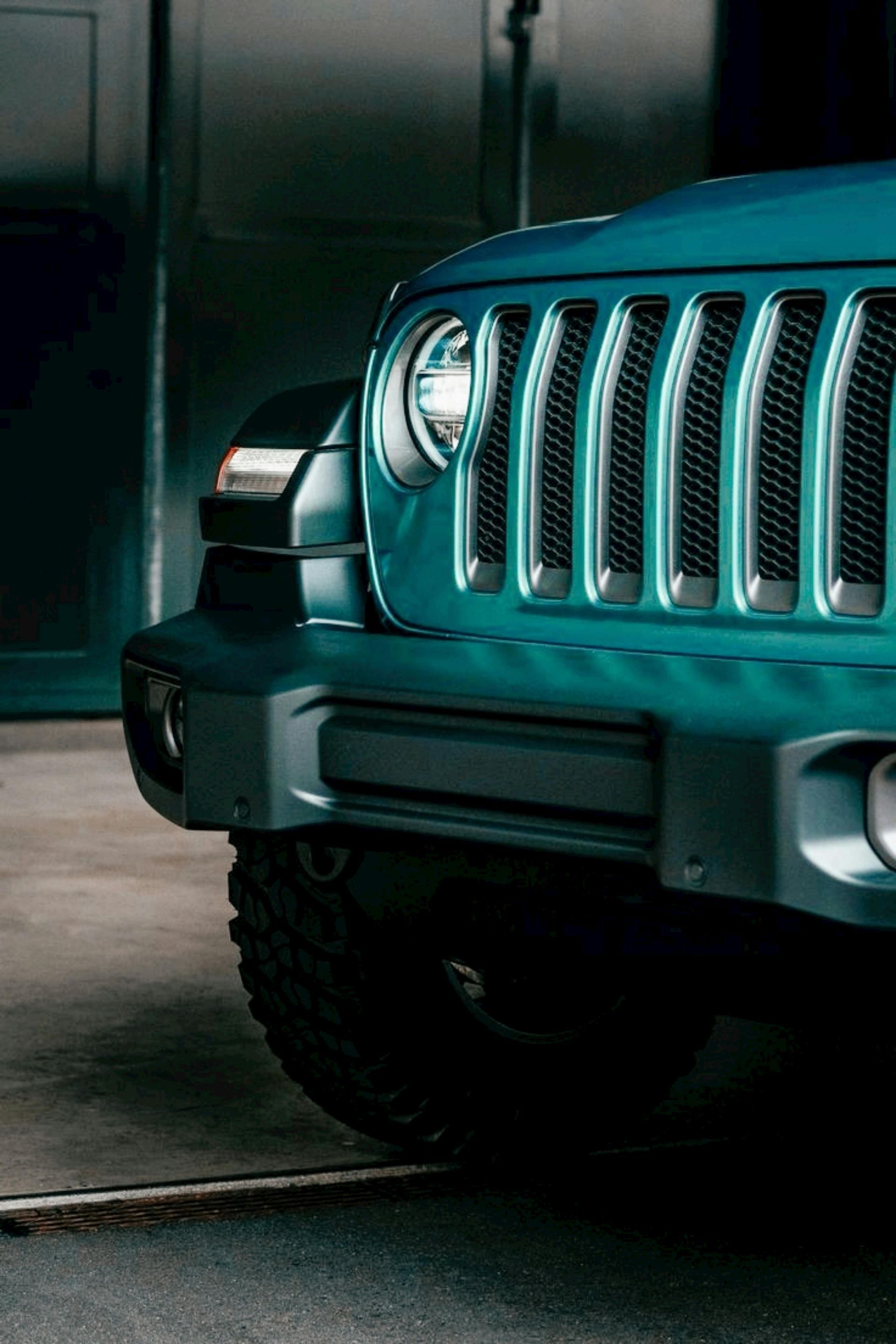 Close-up of a teal SUV front grille and headlight in a garage.
