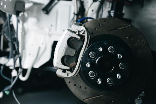 Close-up of a vehicle's disc brake assembly with a silver caliper mounted on a dark, drilled and slotted brake rotor.