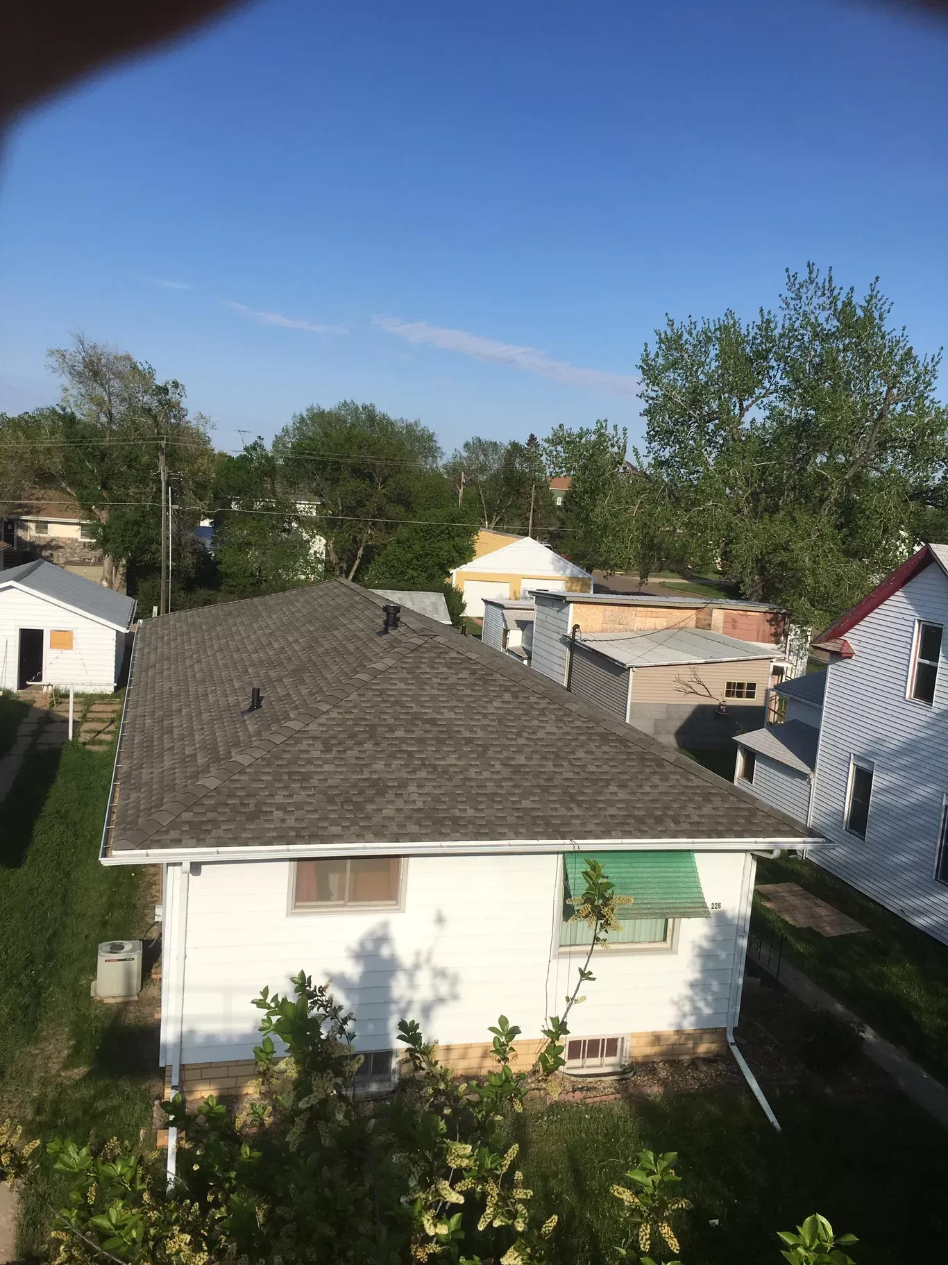 View of several white houses with gray roofs under a clear blue sky. Green trees and grass surround the buildings.