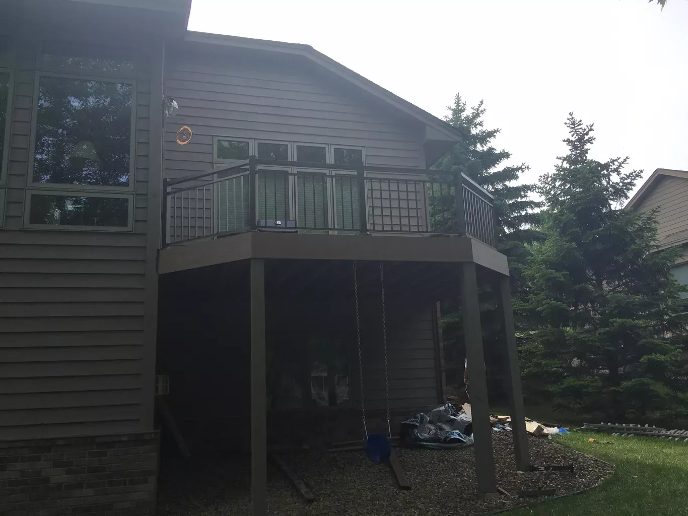 A two-story house with a wraparound deck. The deck has black metal railings and is accessible from glass doors on the second floor.