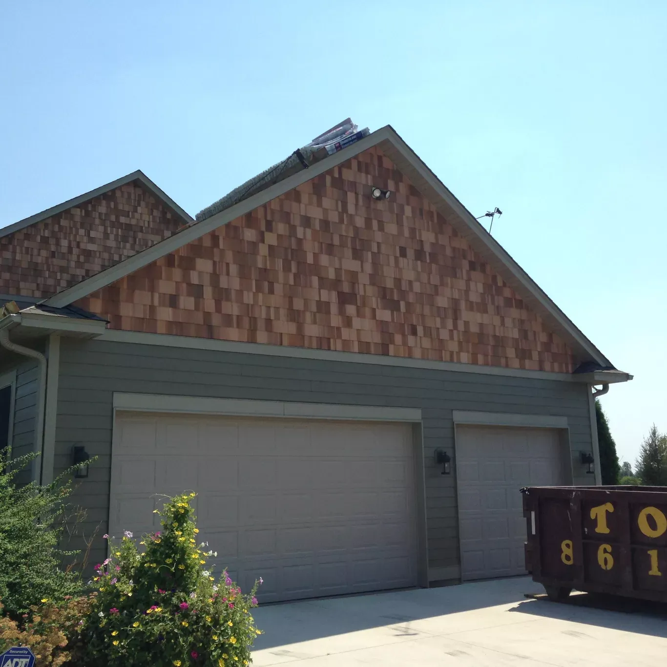 Garage with two doors, light green siding, and brown shingle siding on the gables. A dumpster is in the foreground.