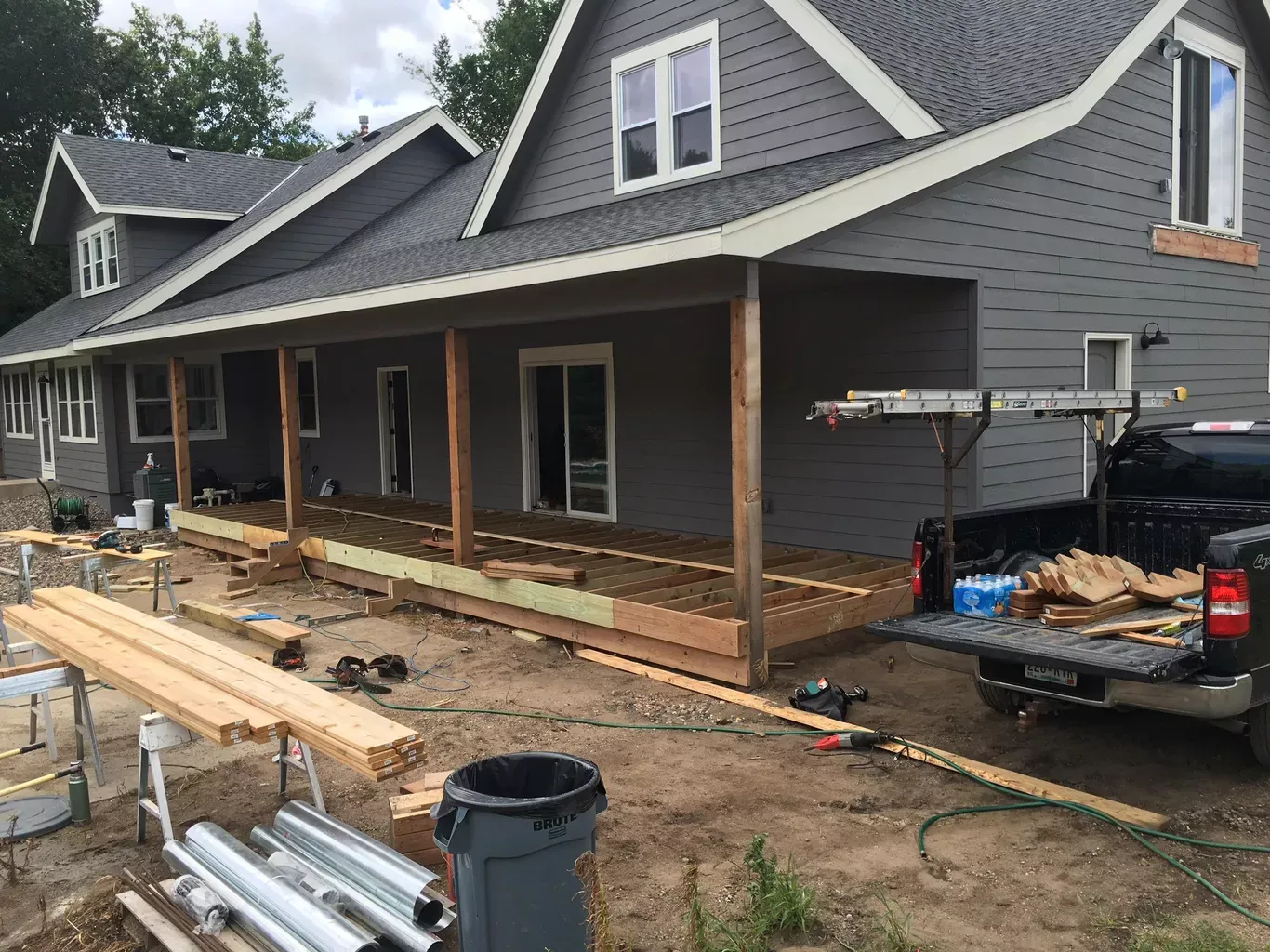 Construction site with a house and a partially built porch. Gray house with white trim, workers building the wooden porch.