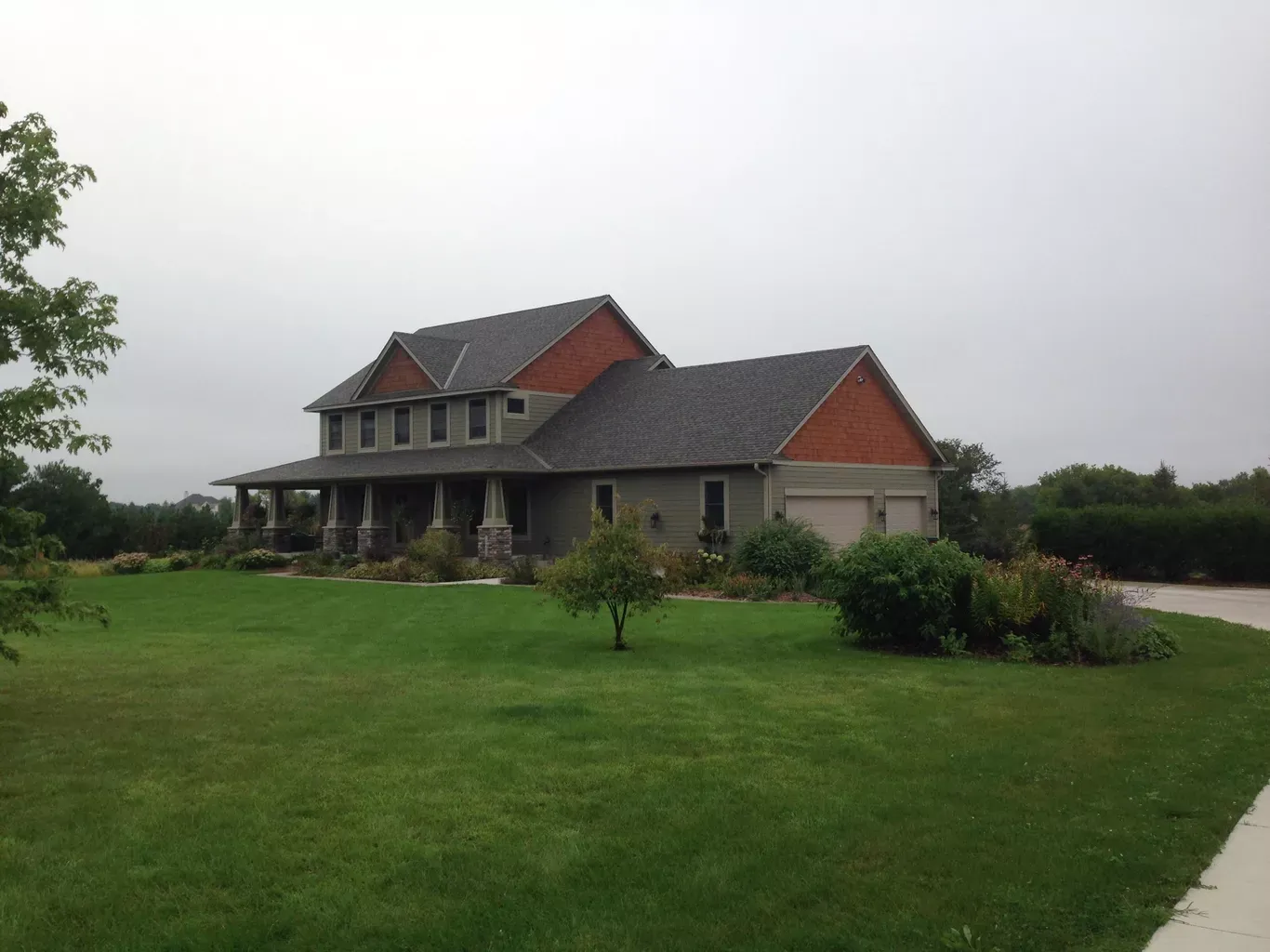 Two-story house with a porch and attached garage on a large green lawn under an overcast sky.