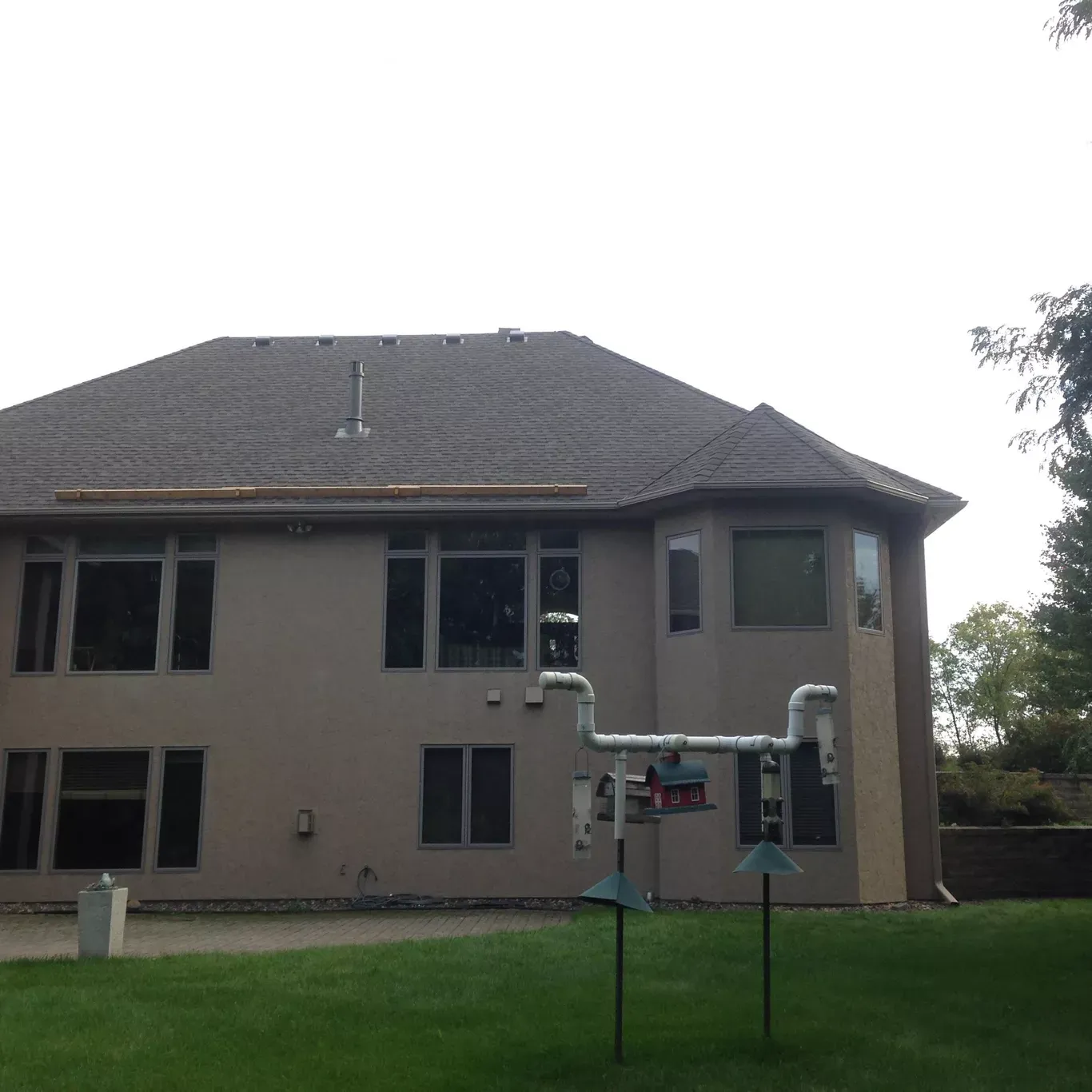 Back of a beige two-story house with dark roof and attached utility equipment on a grassy lawn.