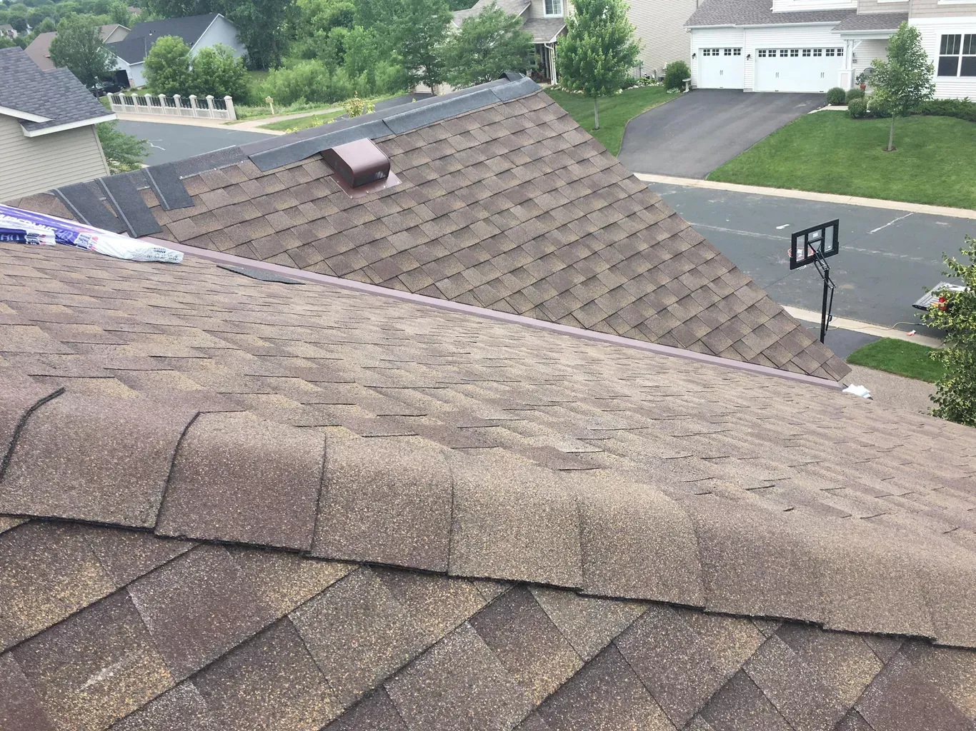 Close-up view of a brown shingled roof. A small vent and some partially installed shingles are visible.