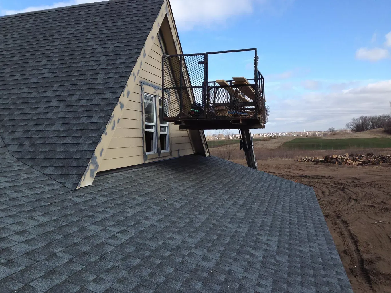A-frame roof with dark shingles, attached to a light-colored building with a small enclosed deck, with a blue sky in the background.