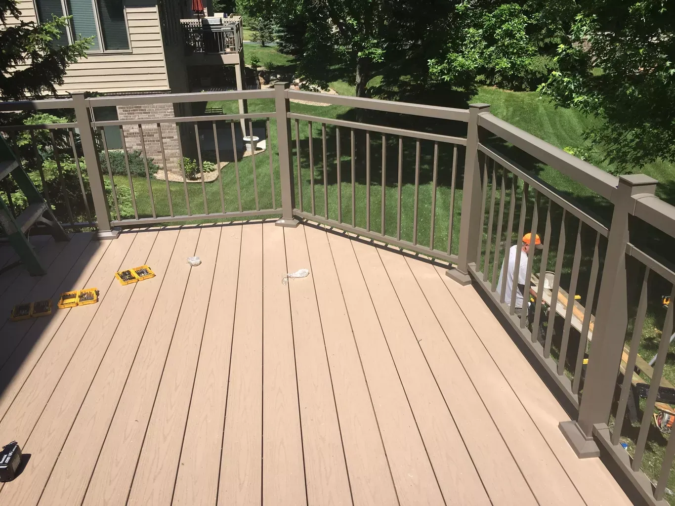 Wooden deck with brown railing overlooking a green lawn. A person is working near the railing.