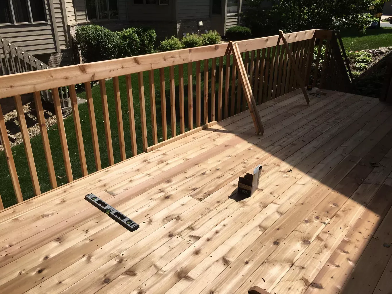 Newly built wooden deck with railings, level, and tools, outdoors on a sunny day.