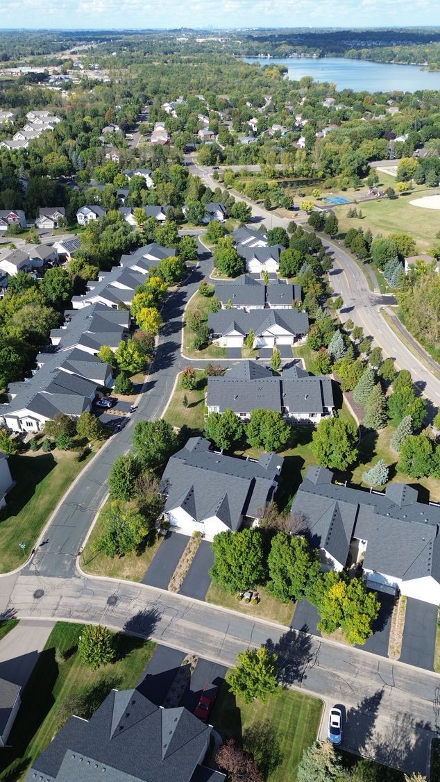 Aerial view of a suburban neighborhood with rows of houses, green trees, and a lake in the distance.