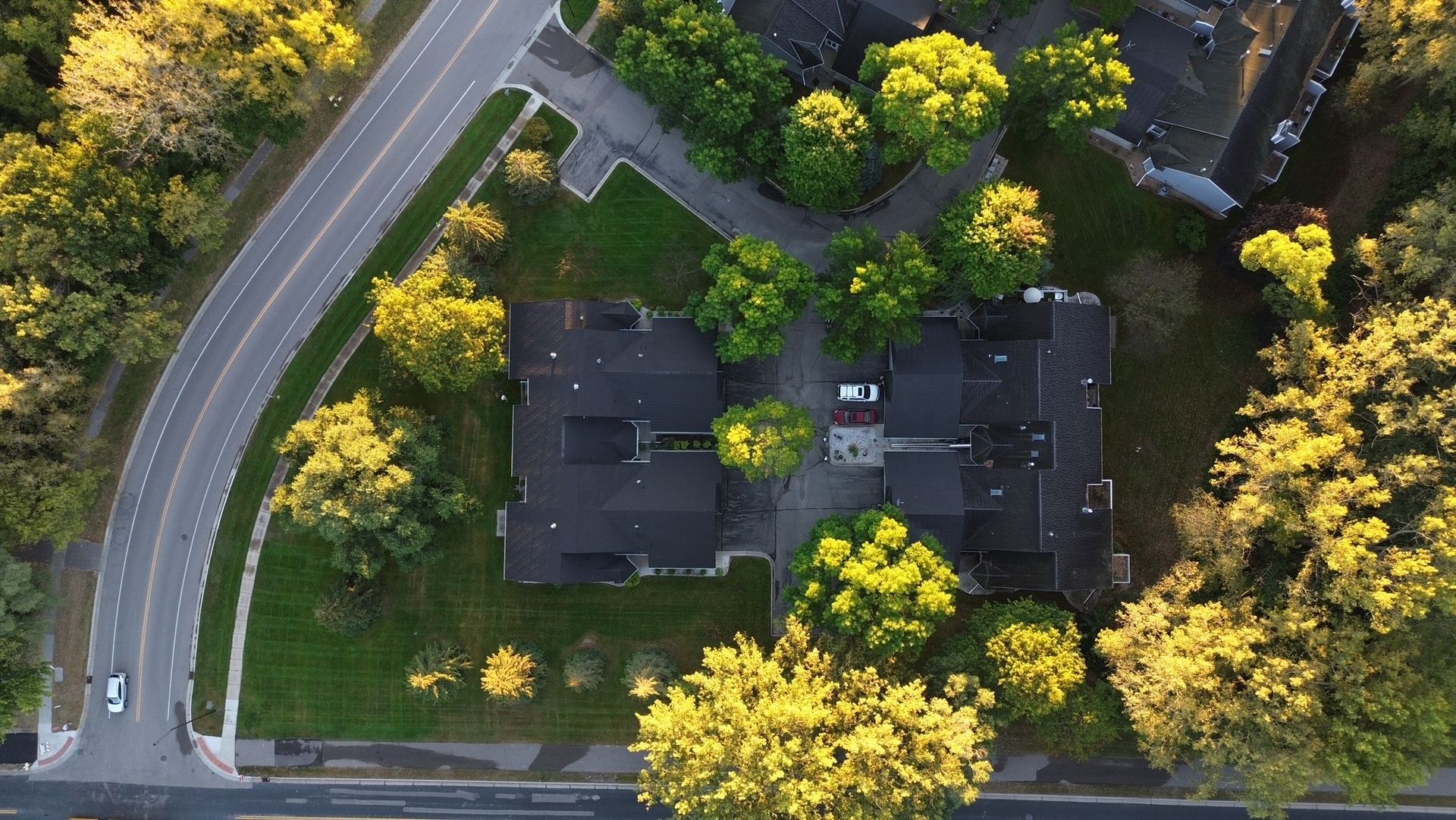 Aerial view of buildings surrounded by trees and grass, next to a curved road.