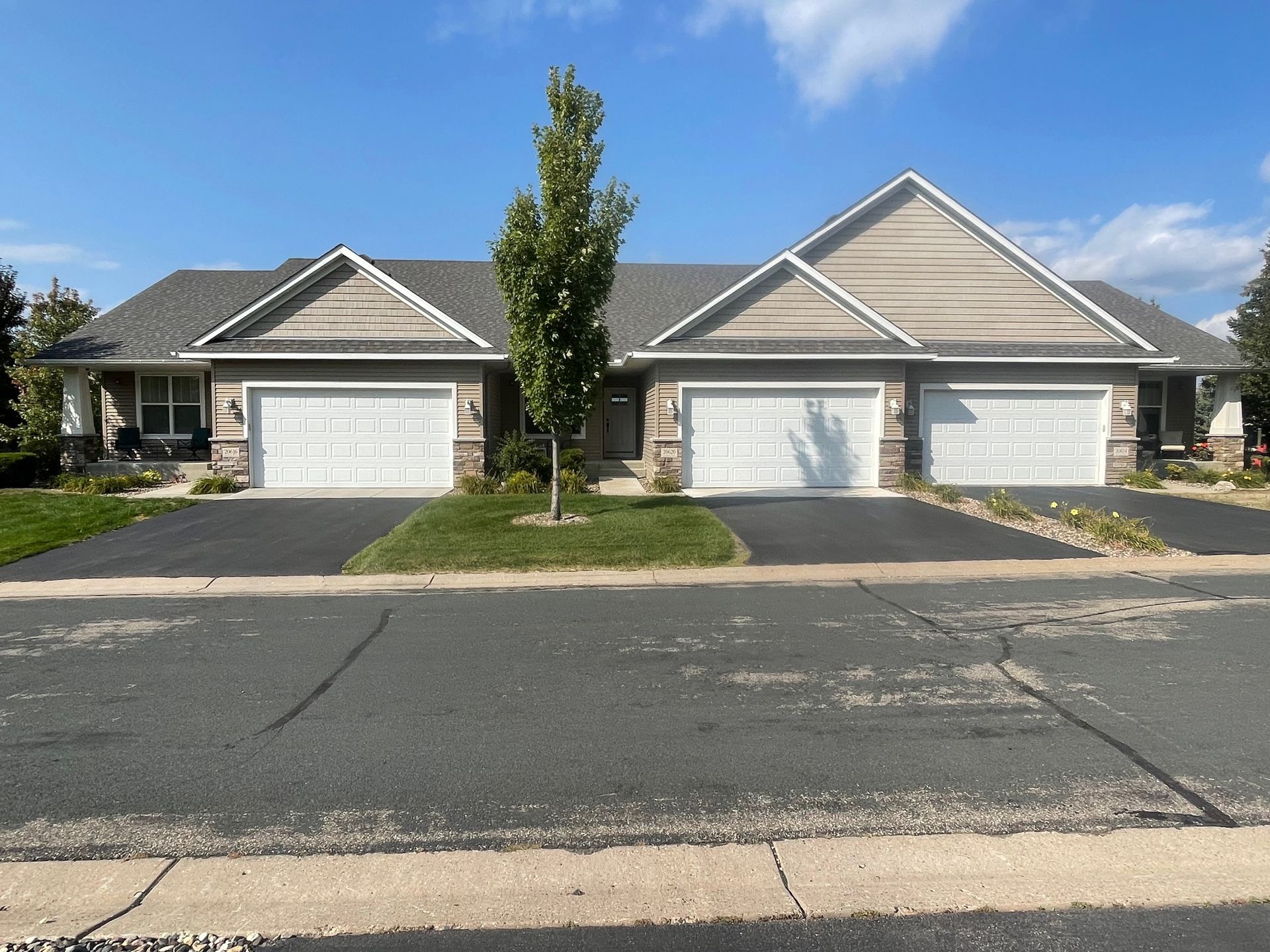 Row of attached houses with three-car garages. Light-colored siding, gray roofs, and asphalt driveways under a bright blue sky.