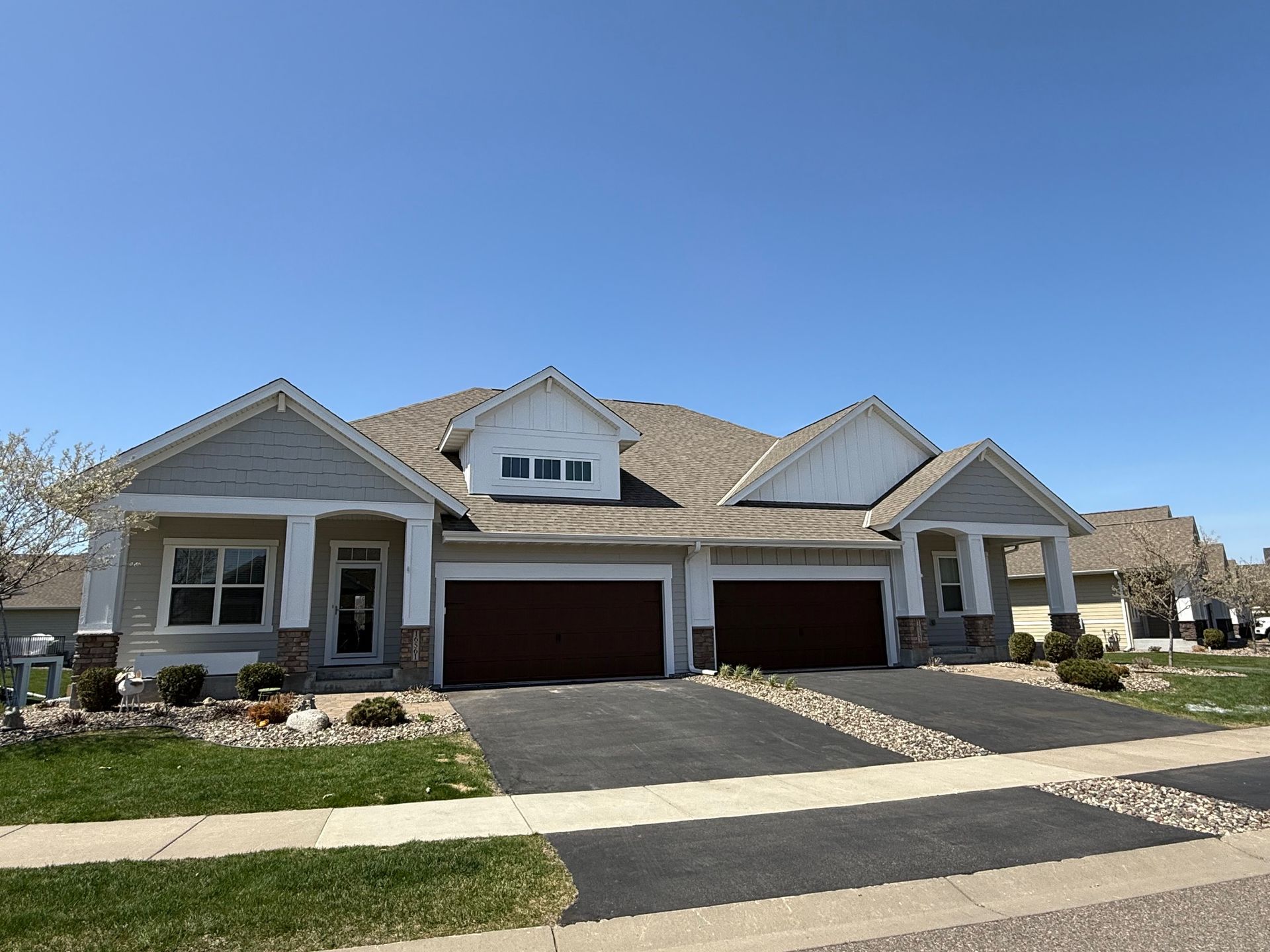 Two-unit townhome with gray siding, brown garage doors, and a blue sky. Each unit has a front door and small front yard.
