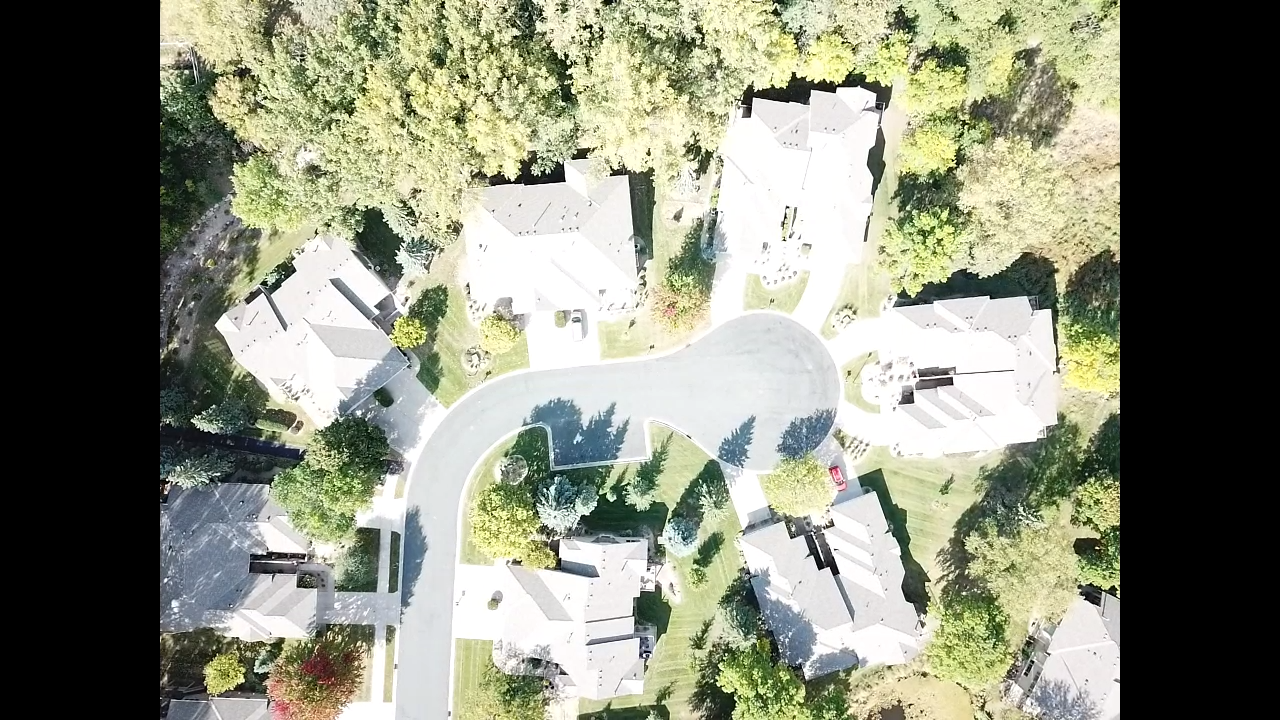 Aerial view of a residential cul-de-sac surrounded by trees. Houses with gray roofs line the street.