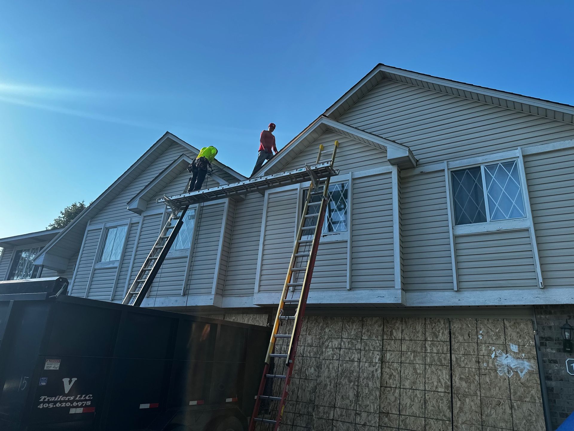 Two workers on ladders installing siding on a two-story building under a clear blue sky.