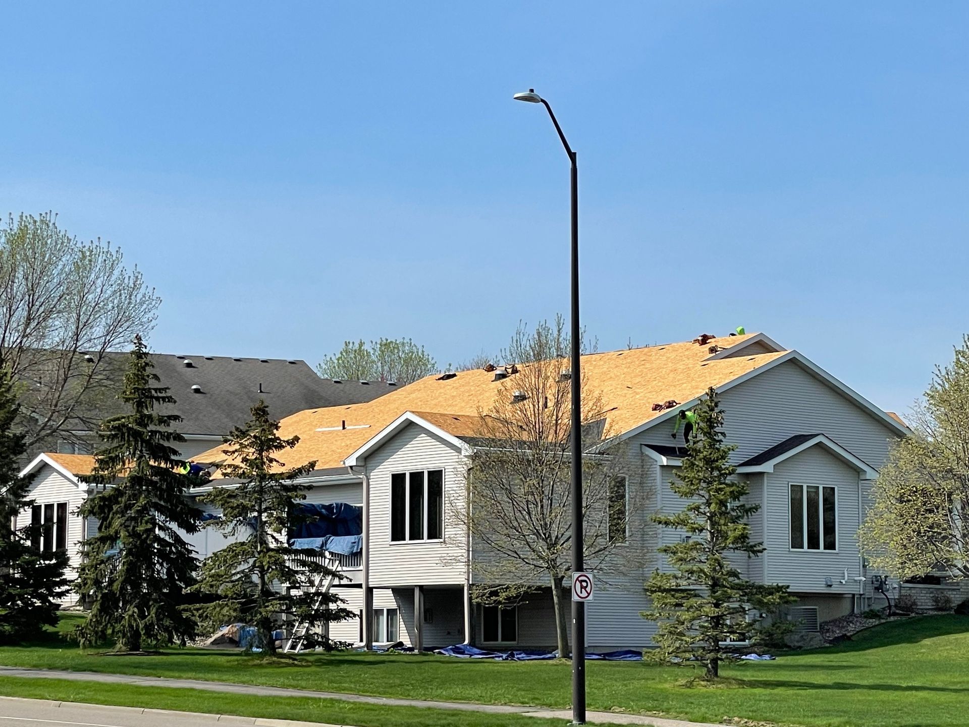 House under construction with exposed roof beams. A black street light stands in front, with greenery and blue sky in the background.