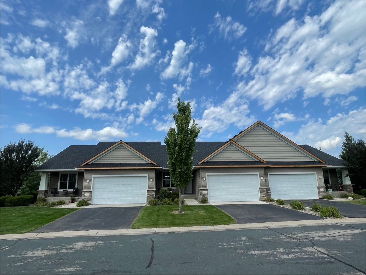 Row of townhouses with white garage doors under a blue sky with clouds. Each has a brown roof and trim.