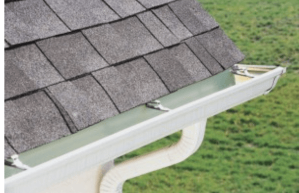 Gray asphalt shingles on a roof edge with a white gutter and downspout.