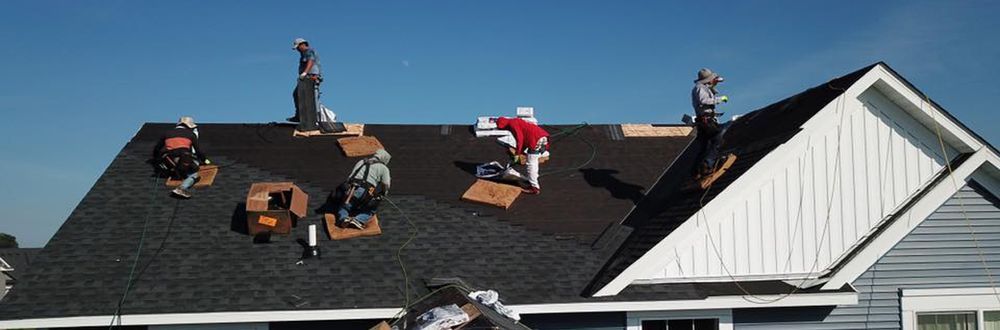 Roofers in various positions working on a roof under a clear blue sky. One roofer is wearing a Santa suit.