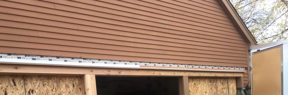 Brown siding on a building with an open space below. Trees visible in the background.