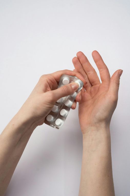 Hands holding a blister pack of white pills, dispensing one into the open palm of the other hand.