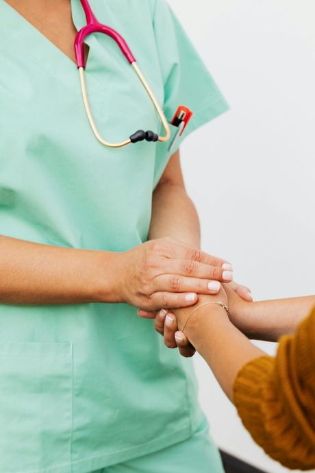 Nurse in green scrubs holding patient's hand for support, stethoscope around neck.