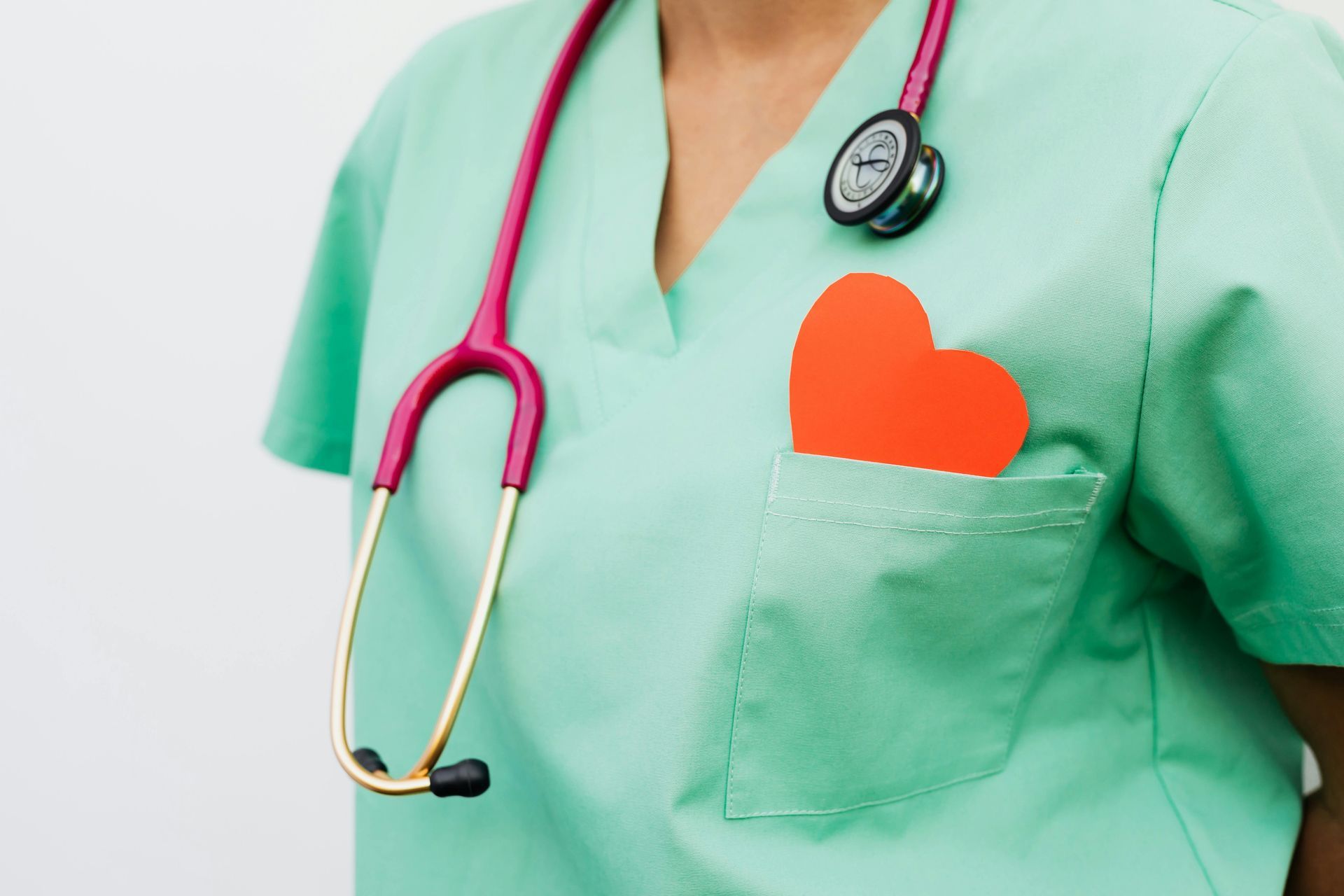 Nurse in green scrubs with stethoscope and red heart in pocket.