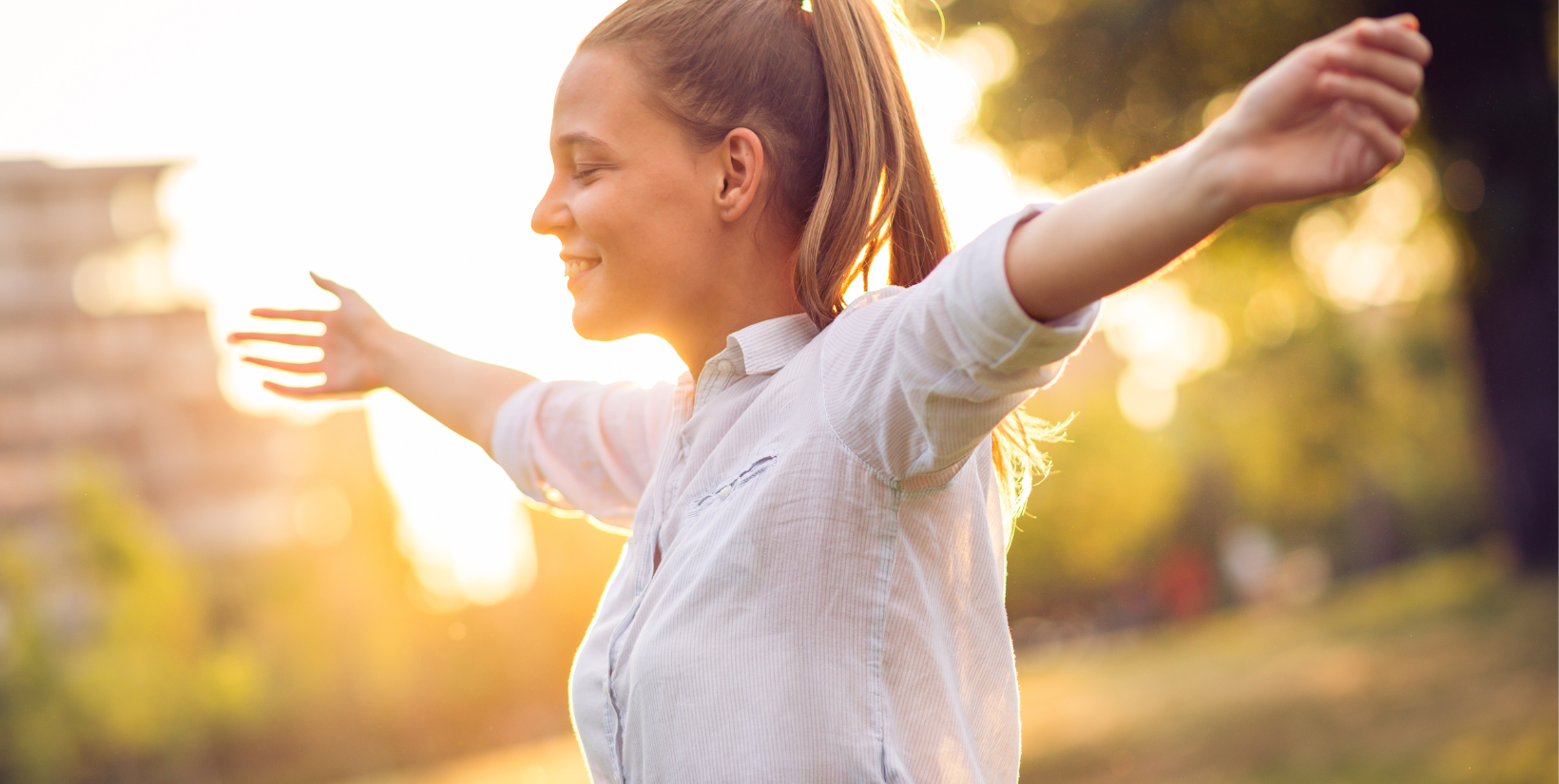 A woman is standing in a park with her arms outstretched.