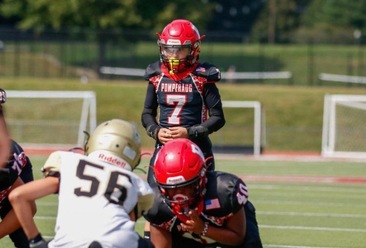 Youth football players in red and black uniforms on a sunny field. Player number 7 stands, focused.