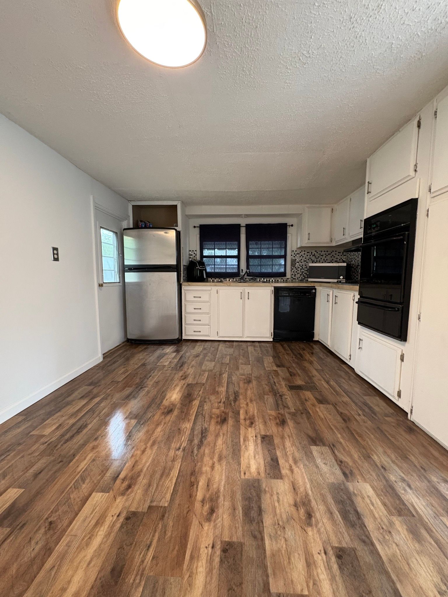 An empty kitchen with hardwood floors and white cabinets.