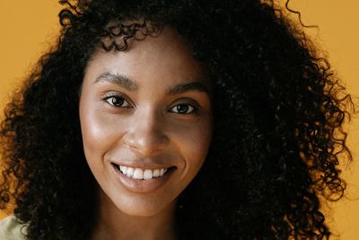 Close-up portrait of a smiling person with curly hair against a warm yellow background