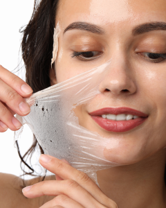 Woman peeling off a translucent facial mask, smiling in a skincare close-up