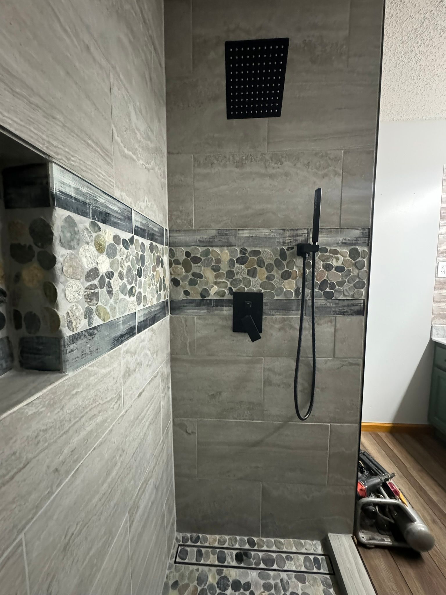 Shower with gray tiled walls, a decorative stone band, and black shower fixtures.