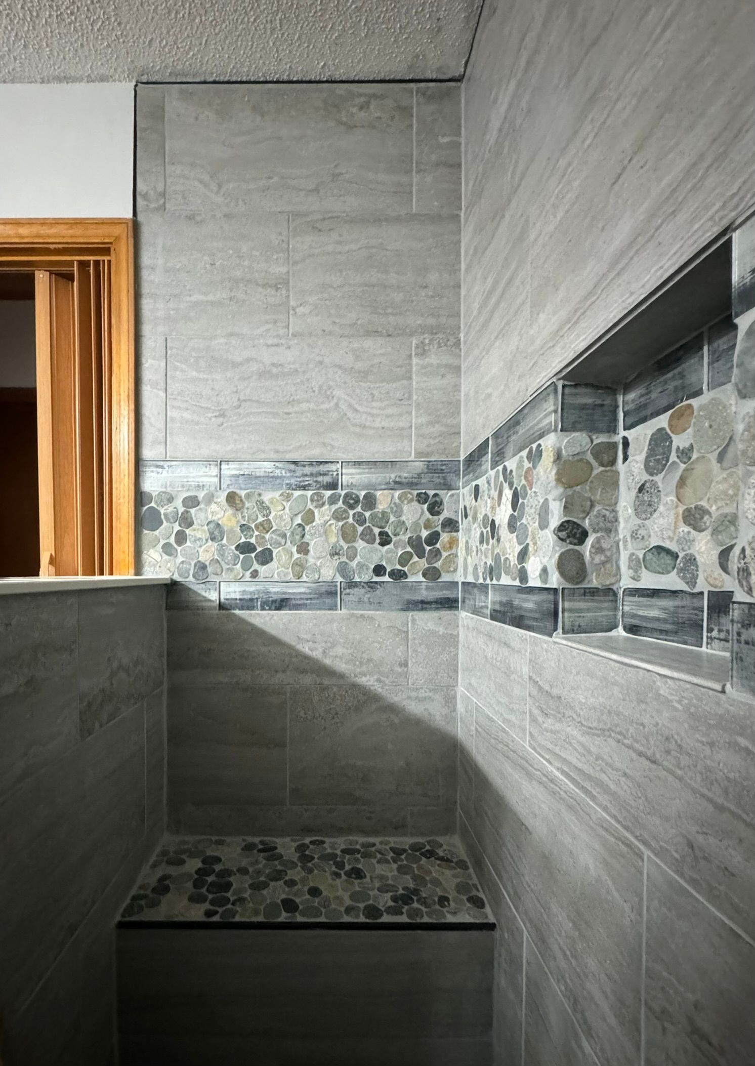 Gray tiled shower with a pebble tile accent and built-in bench.