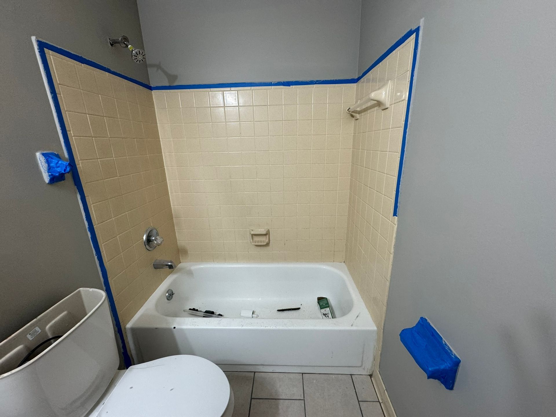Bathroom with beige tiled shower stall, tub, toilet, and gray walls, taped for painting.