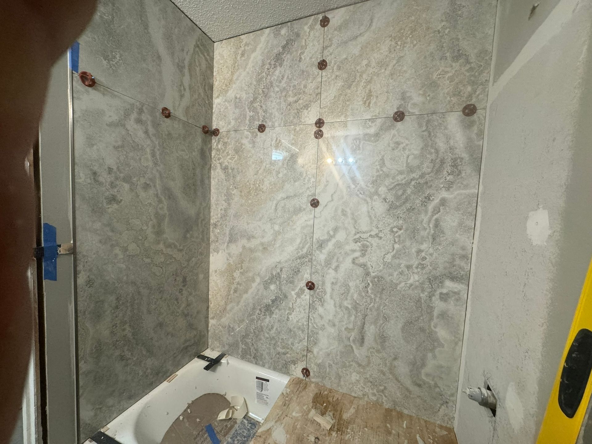 Bathroom tiling in progress; gray marble-look tiles installed on wall above a bathtub.