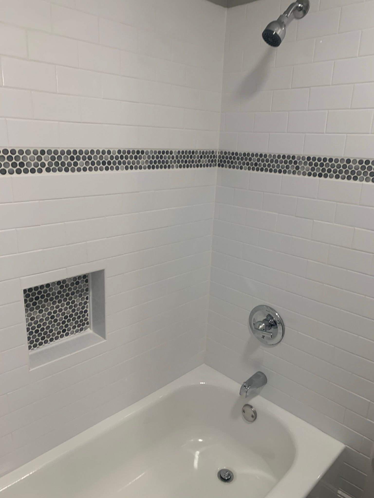 White tiled shower with mosaic accent, built-in niche, and chrome fixtures.