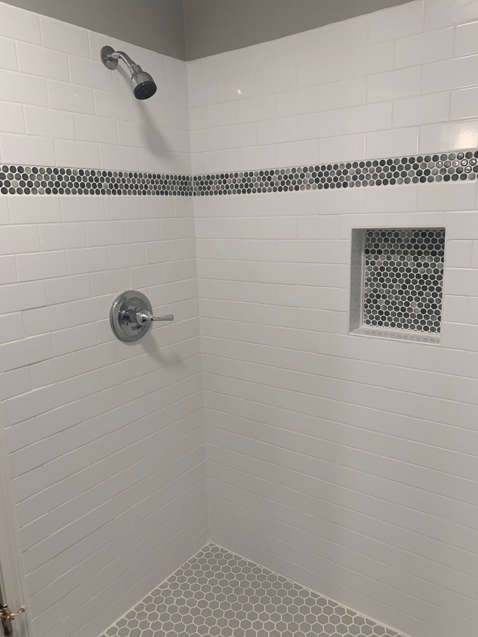 White-tiled shower with mosaic accents, chrome fixtures, and a recessed shelf.