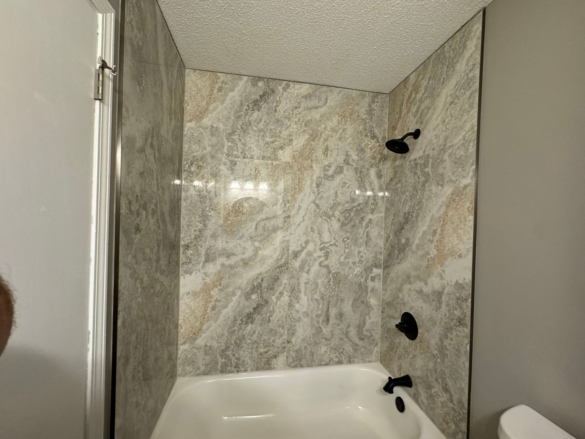 Bathroom shower with marble-patterned walls, black fixtures, and a white bathtub.