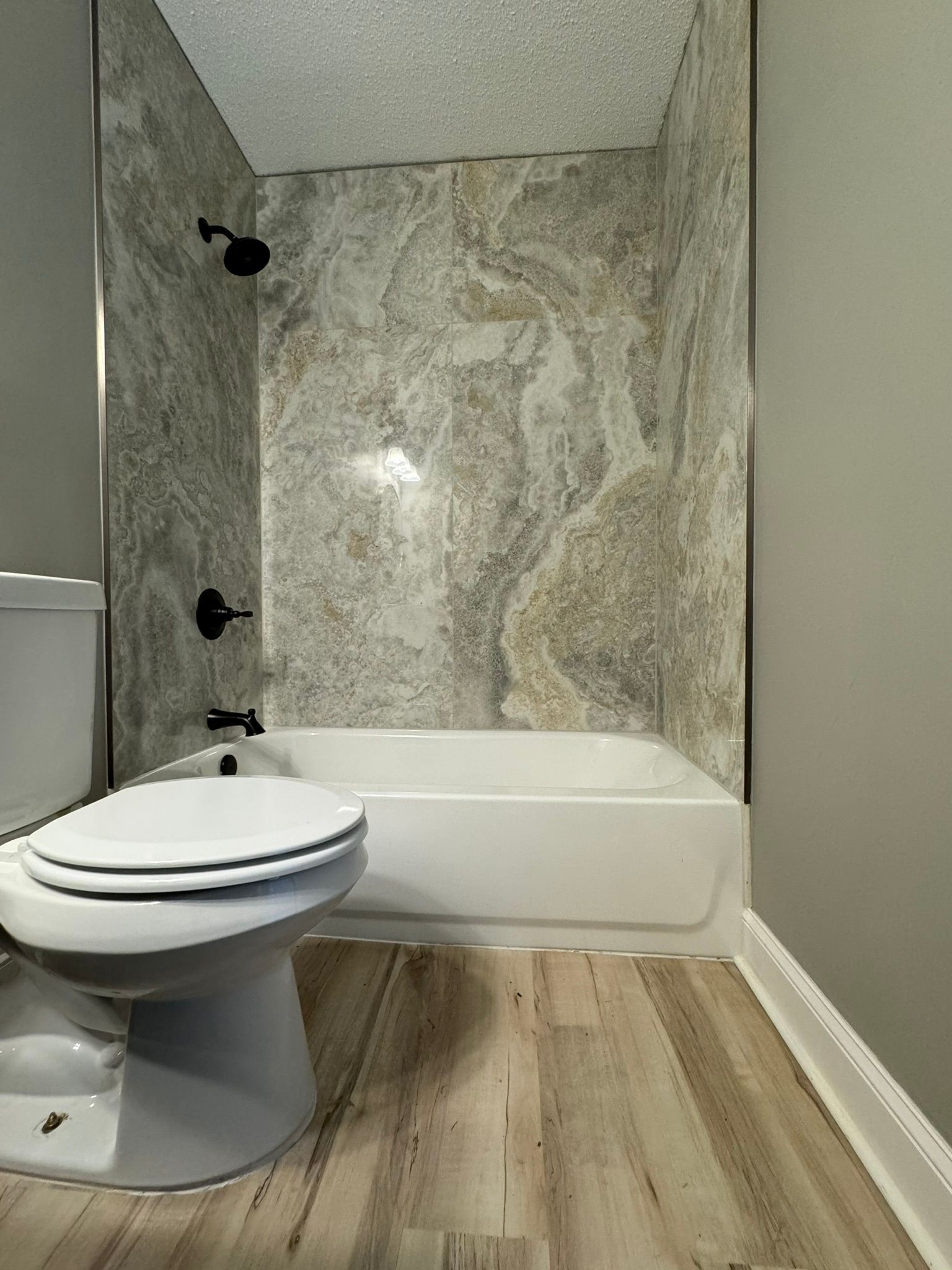 Bathroom with white toilet and tub, shower with black fixtures, and gray and beige walls.
