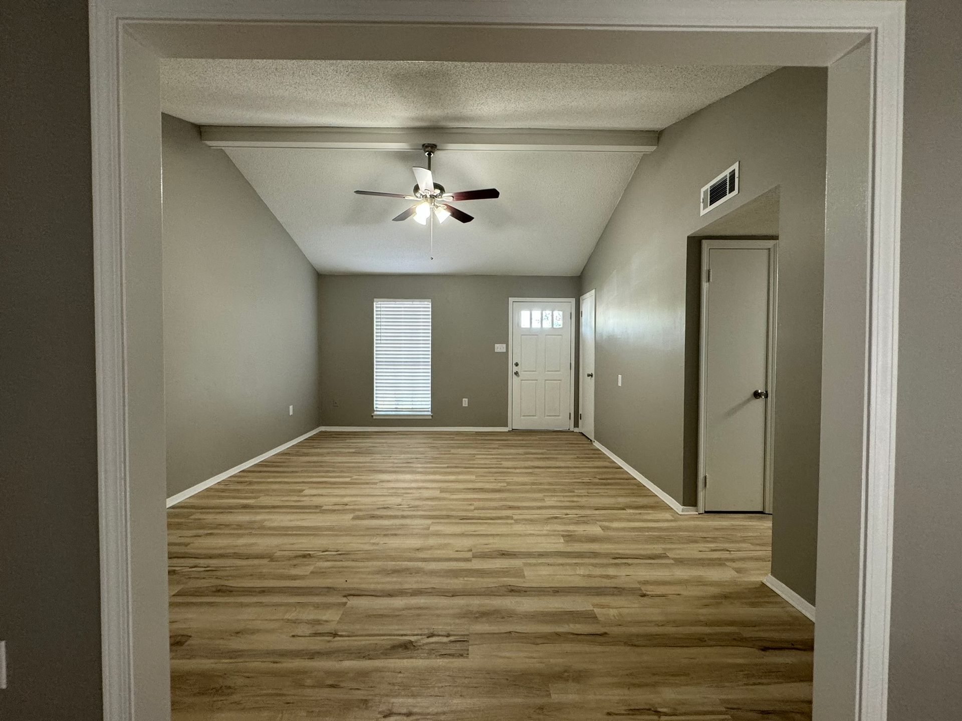 Empty room with wood-look floors, grey walls, and white trim, viewed through a doorway.