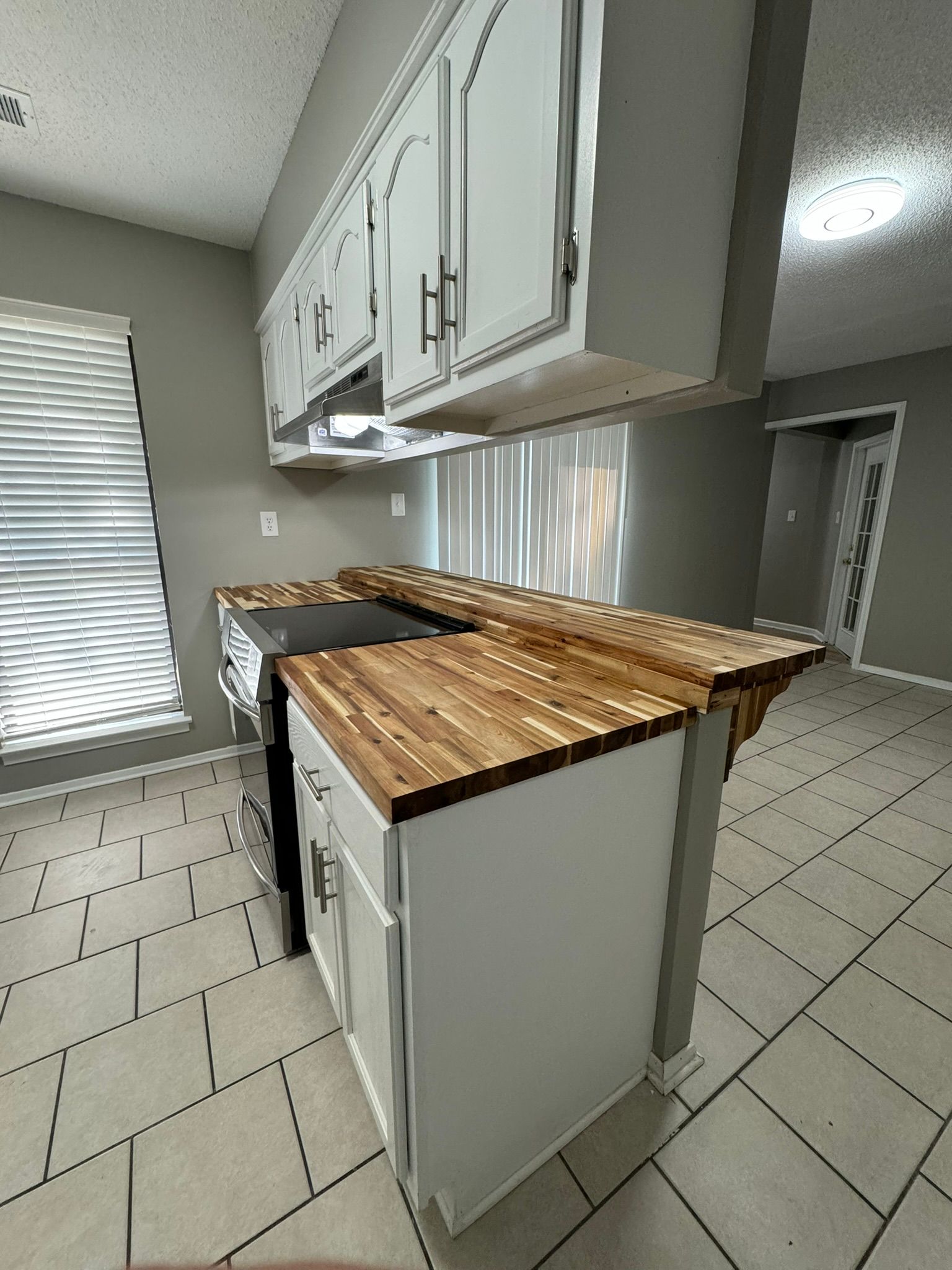 Kitchen with white cabinets, wood countertops, and gray walls; a stove and window are visible.