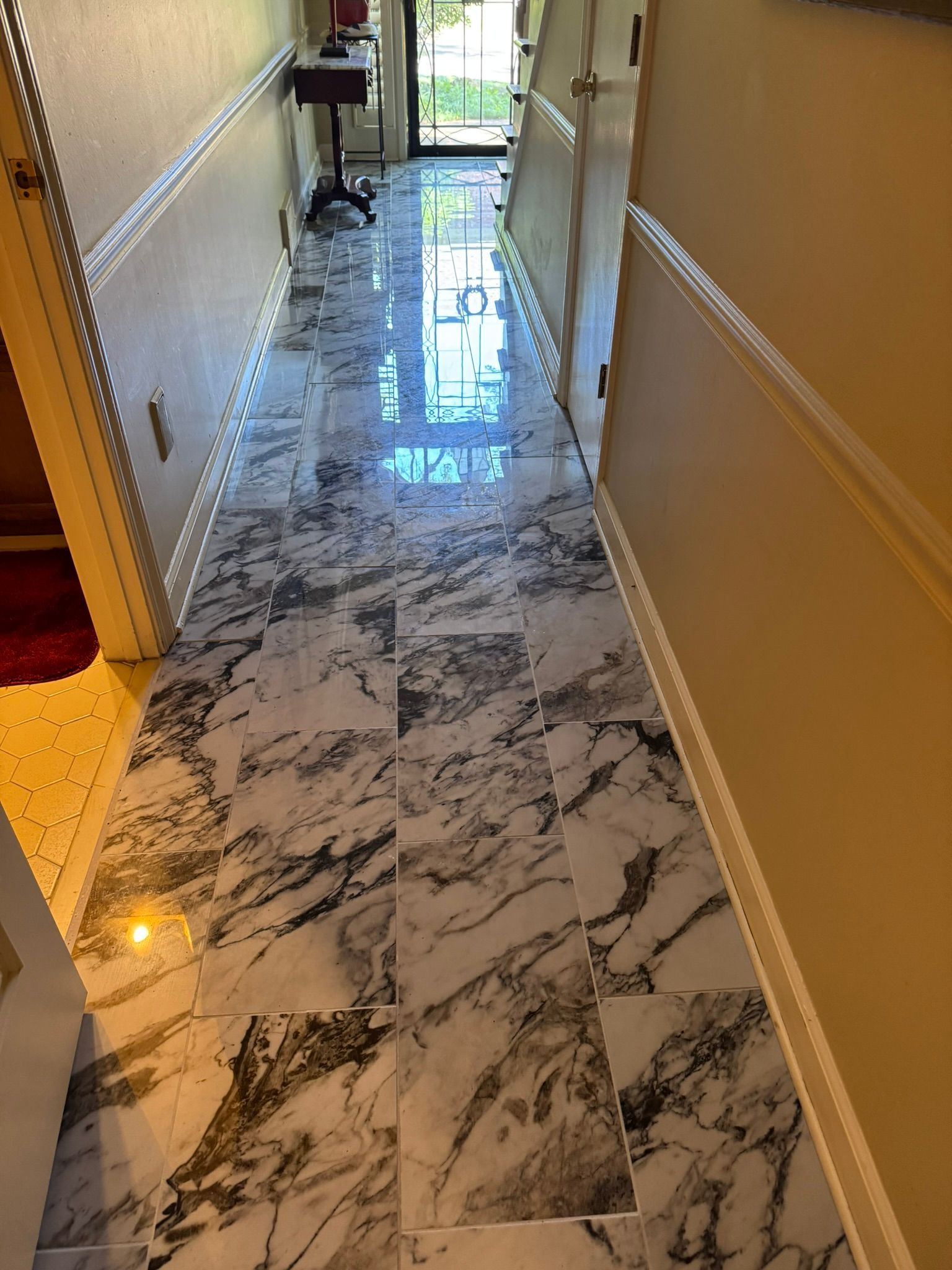 Long hallway with marble-patterned floor, white walls, and a door at the end; bright sunlight streams in.