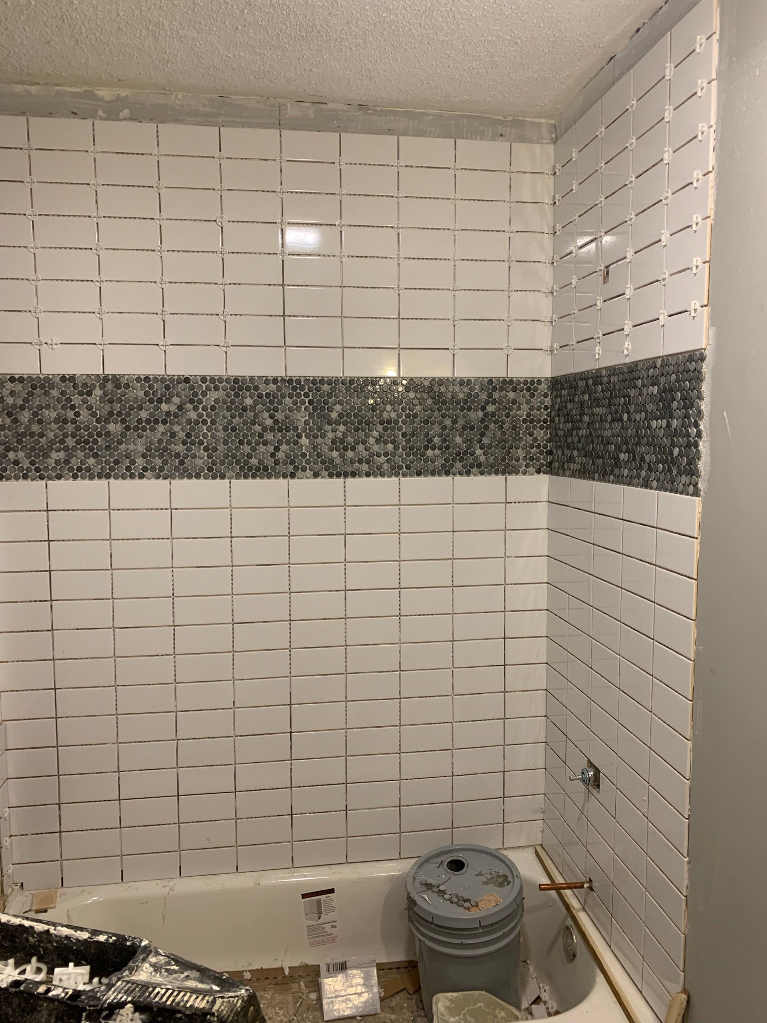 Bathroom with white and gray tile in progress. Tub and bucket are visible.
